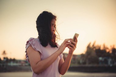 Kadın portresi Smartphone kullanarak Beach sırasında gün batımında, Asya turizm rahatlatıcı ile Her cep telefonu on Beach Tatil zamanı. Teknoloji iletişim kavramı.