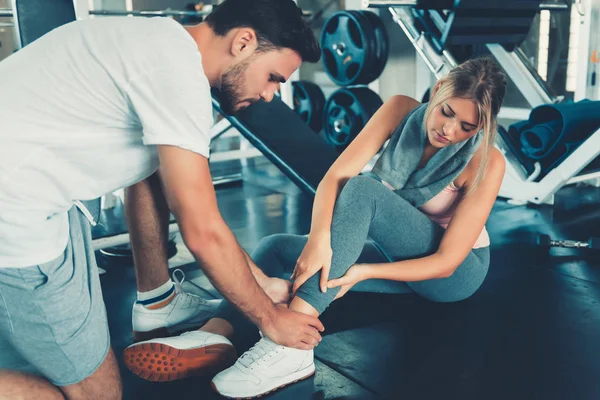 Pretty Woman Having Injury During Exercise in Gym While Her Couple Taking First Aid, Accident and Sport Fitness Concept.
