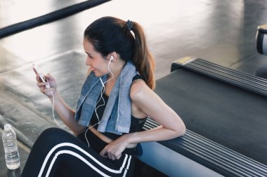 Sportif kadın fitness club., spor, spor ve boş zaman faaliyetleri kavramı egzersiz sırasında kulaklık ile müzik dinlemek Asyalı kadın portresi treadmill egzersiz sonra smartphone kullanıyor.