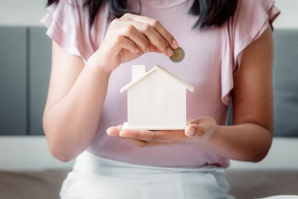 Großaufnahme Frau Hand steckt eine Geldmünze in Gehäuse auf dem Schlafzimmer., weibliche Hand steckt Münze in Haus sparen. Business Banking und Finanzkonzept. — Stockfoto