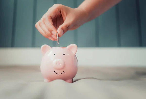 Woman Hand is Putting a Money Coin into Piggy Saving on The Bedroom., Female Hand is Inserting Coin in Piggybank., Business Banking and Financial Concept.