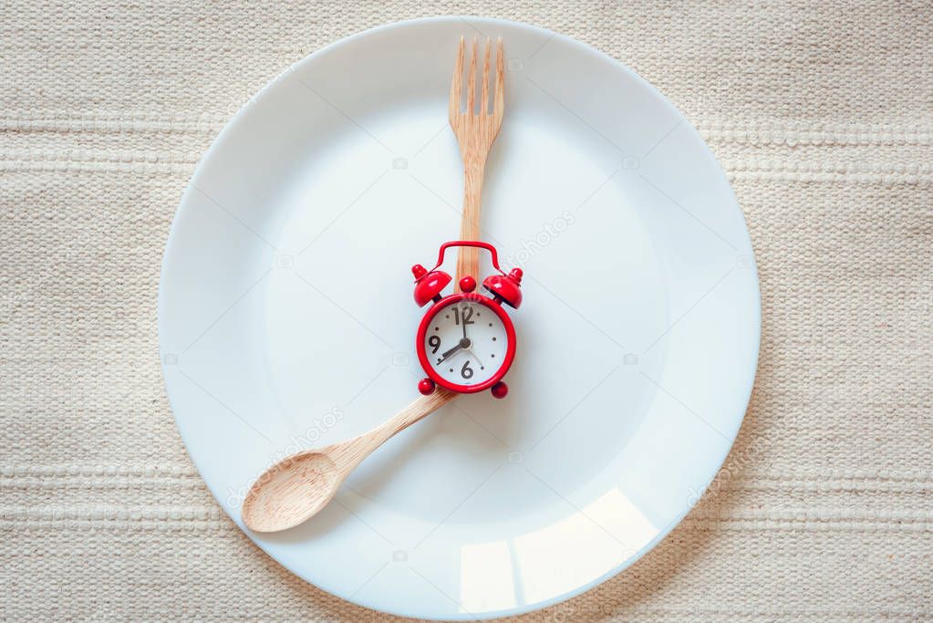 Healthy Eat Meal Time and Reminder Breakfast Concept, Food Timing Cycles for Eating, Red Alarm Clock With Wooden Spoon and Fork on Ceramic Dish. Empty Plate and Household Object on a Table, Food Idea.