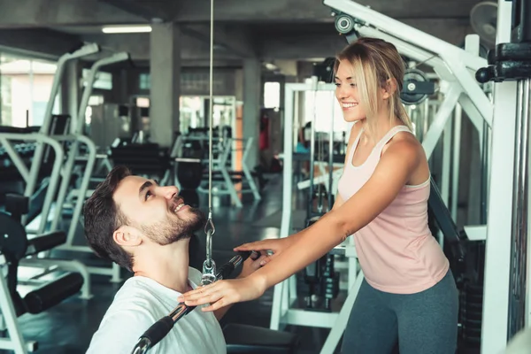 El retrato del hombre guapo es entrenamiento ejercitado con la máquina del culturista en el club de la aptitud., atractivo del hombre deportivo que hace ejercicio con su instructor en el concepto del gimnasio, del estilo de vida sano y del deporte . — Foto de Stock