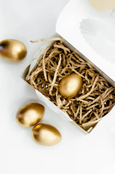 Ovos de Páscoa dourados em uma caixa com estrelas douradas sobre fundo branco. Páscoa férias conceito abstrato fundo copyspace vista superior — Fotografia de Stock
