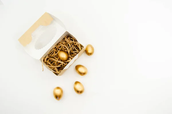 Ovos de Páscoa dourados em uma caixa com estrelas douradas sobre fundo branco. Páscoa férias conceito abstrato fundo copyspace vista superior — Fotografia de Stock
