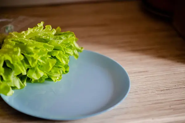 Verse groene sla bladeren op een blauwe schotel. Glettuce op een plaat bruin houten tafel. — Stockfoto