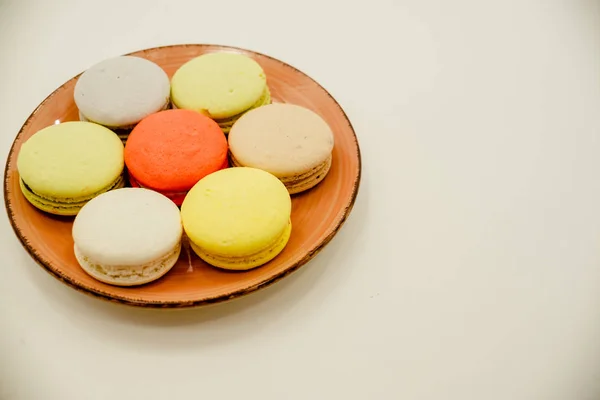 Colección de coloridos macarrones franceses están uno al lado del otro en un plato azul sobre fondo blanco —  Fotos de Stock