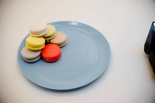 Colección de coloridos macarrones franceses están uno al lado del otro en un plato azul sobre fondo blanco —  Fotos de Stock