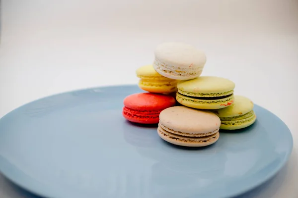 Colección de coloridos macarrones franceses están uno al lado del otro en un plato azul sobre fondo blanco —  Fotos de Stock