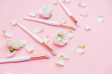 Beyaz arka planda makyaj fırçaları ve çiçekler. Yatay görünüm telif uzayı.