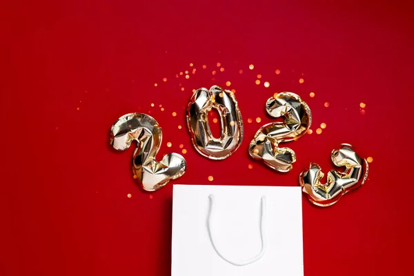 Palloncini di lamina d'oro 2021 con una borsa su sfondo rosso festivo con bokeh. Vista orizzontale superiore copyspace. Nuovo anno e concetto di shopping natalizio. — Foto Stock