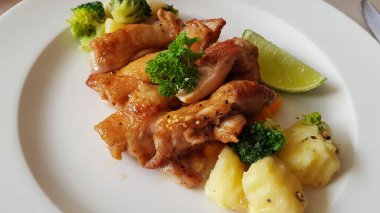 Beyaz tabakta sebzeli ızgara tavuk parçaları. Bir parça kireç.