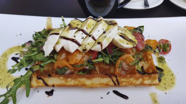 Mozzarella ve roka dilimleri ve domatesli waffle. Balzamik sosa bulanmış..