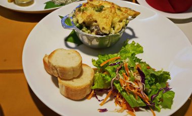 Fırında jülyen, dilimlenmiş baget, doğranmış salata. Beyaz tabakta yemek