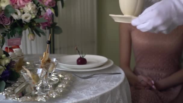 El camarero con guantes blancos pone en la mesa delante de la chica una taza de té . — Vídeos de Stock