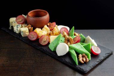 Siyah şeyl üzerinde peynir tabağı. Meyve parçaları.