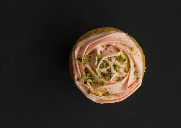 Cup cake top view photo with pink swirled icing isolated on black background with space for text