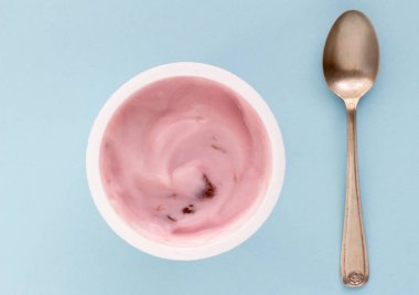 Plastik bardak yoğurt yakın çekim küçük gümüş kaşık, üstten görünüm fotoğraf soluk mavi zemin üzerine çilekli yoğurt ile