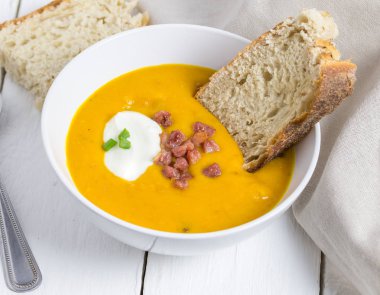 Butterrnut ve pastırma çorbası ekşi krema, pastırma bit ile tepesinde ve scallon ciabatta ekmeği ile yakın çekim rustik beyaz masa üstü