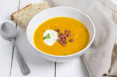 Butternut ve pastırma çorbası ekşi krema, pastırma bit ve yeşil soğan Tepesi ekmek ile beyaz rustik masada beyaz kase