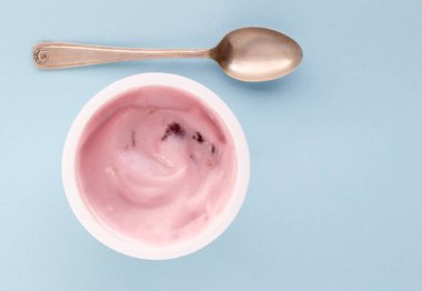 Plastik bardak yoğurt yakın çekim küçük gümüş kaşık, üstten görünüm fotoğraf soluk mavi zemin üzerine çilekli yoğurt ile