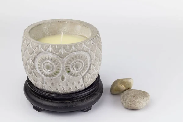Candle holder with wax unlit candle depicting an owl on white background with two pebbles next to it