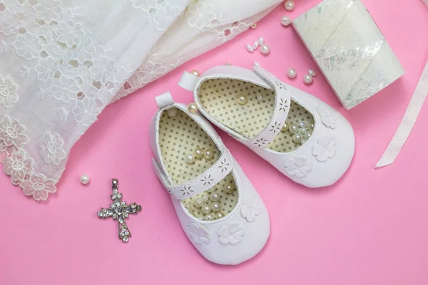 Baptism dress, shoes, crystal cross pendant, pearls and little mother of pearl box isolated on pink background - top view photo of baby girl's christening objects