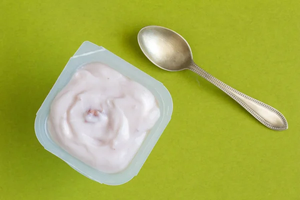 Yogurt cup with strawberry yoghurt and small silver spoon close up - Top view photo of yoghurt on green background