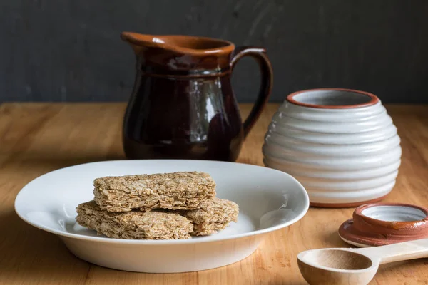 Breakfast cereal bars in bowl, with milk and honey jar in backgr — Stock Photo, Image