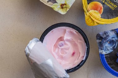 Üç açılmamış yoğurt ile keten arka plan üzerinde siyah plastik fincan çilek yoğurt