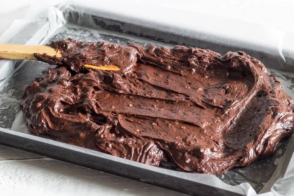 Chocolate brownie cake batter being placed in wax paper lined baking pan — Stock Photo, Image