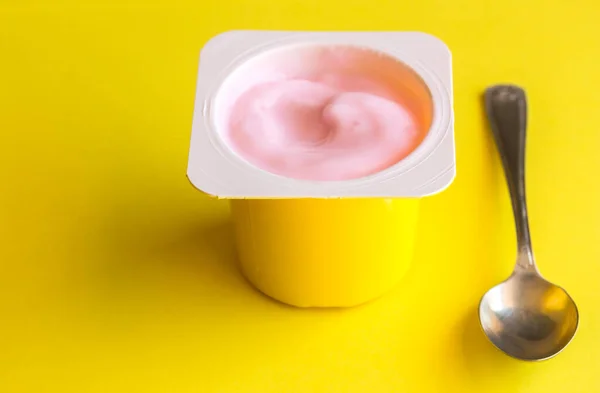 โยเกิร์ตสตรอเบอร์รี่สีชมพูในถ้วยพลาสติกสีเหลืองแยกกันบนพื้นหลังสีเหลืองสดใส — ภาพถ่ายสต็อก