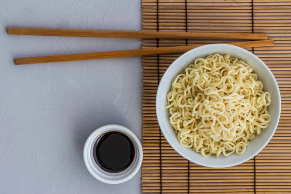 Bowl of plain cooked noodles with chopsticks and little bowl of soy sauce - top view