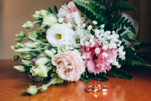 A wedding bouquet of roses. Gold rings on the table.