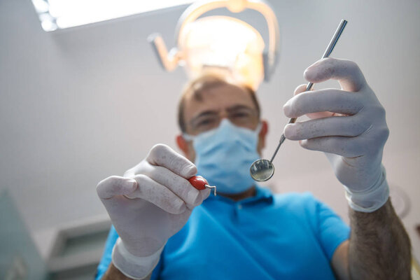 From below shot of man in uniform and gloves using tools and doing oral cavity inspection in dental cabinet.