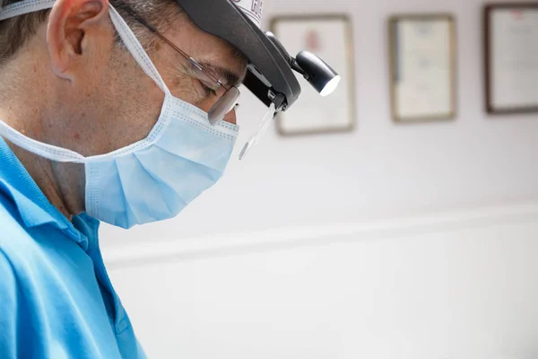 Aydınlatma gözlük takan ve konsantrasyon kliniği ile çalışma ciddi profesyonel diş hekimi yan görünüm. 