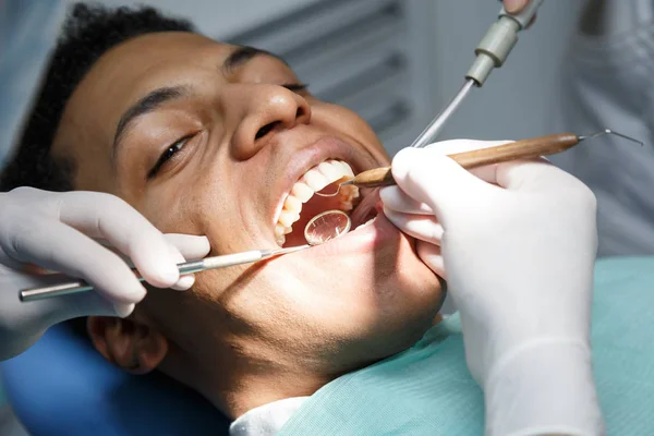 Afrikalı-Amerikalı gencin asistanıyla diş kliniğinde çalışan oral kavite inceleyerek diş hekimi.