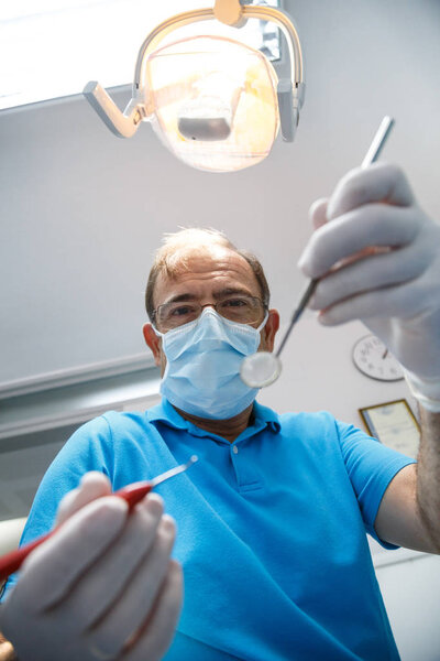 From below shot of dentist in uniform and gloves using tools and doing oral cavity inspection in dental cabinet.