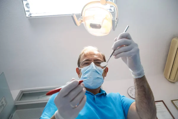 Aşağıdan bir dişçi üniforma ve araçlarını kullanarak ve ağız boşluğu muayene diş dolabında işi eldiven atış.
