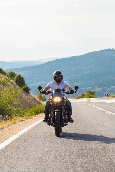Genç adam dağlarda yolda güneşli bir günde bir motosiklet sürme. 