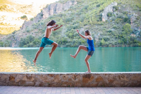 Side view of young people jumping and doing yoga on embankment at turquoise lake