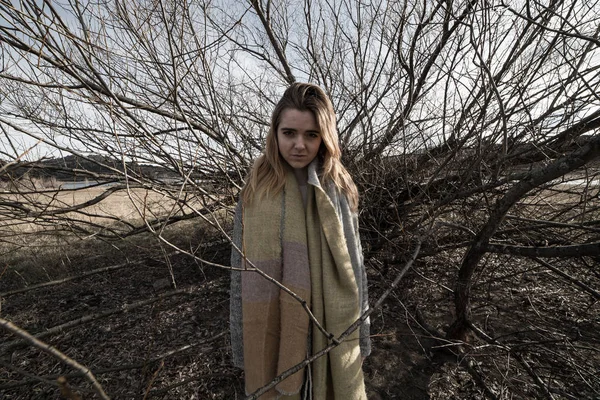 Young woman under the dark shadow of a tree with many branches that produces a scary aesthetic