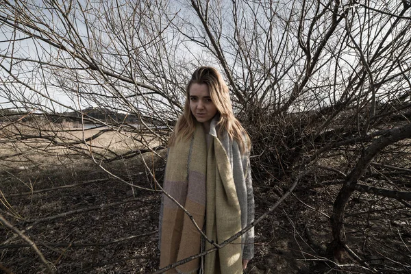 Young woman under the dark shadow of a tree with many branches that produces a scary aesthetic