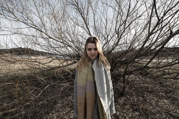 Young woman under the dark shadow of a tree with many branches that produces a scary aesthetic