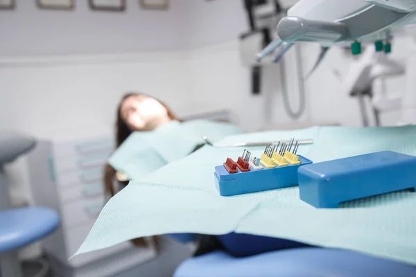 口の清掃とフォーカスに虫歯を除去するため器械装置とソフト フォーカスのクリニック ルームで歯科の椅子に座っている若い女性 — ストック写真