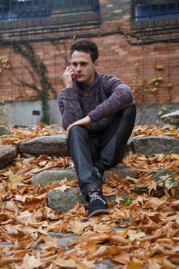 Genç yakışıklı bir rock ile yeşillik çayır üzerinde oturan ve smartphone ile konuşan adam