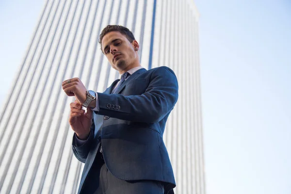 From below view of stylish man in elegant suit posing confidently on background of modern office skyscraper