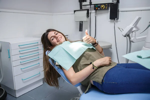 Bir diş kliniği el başparmak sandalyede oturan mavi gözlü genç bir kadın portresi