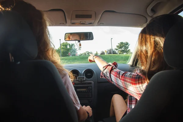 Young women sitting in the front seats of the car pointing where to go on a vacation trip.
