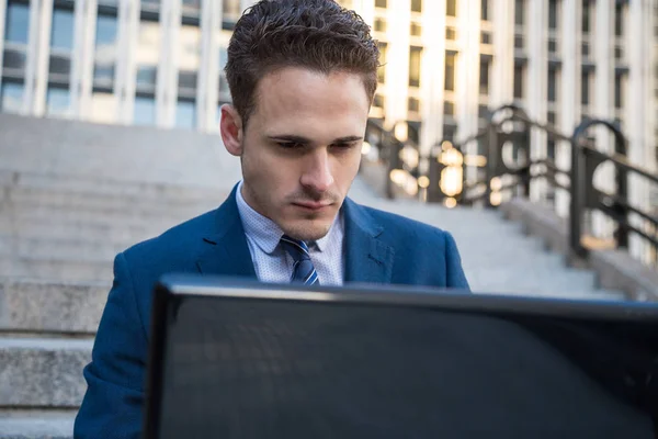 Portrait of man in elegant suit working on stairs with laptop on knees.